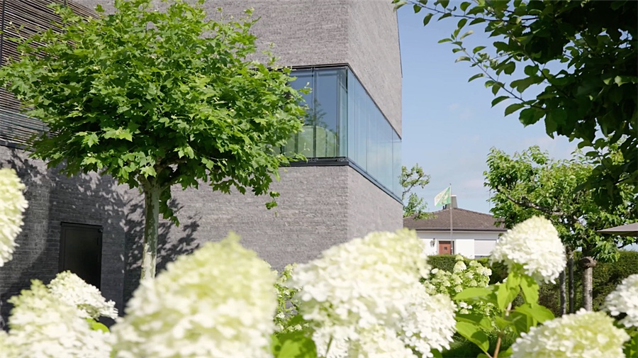 Rahmenlose Glasecke des Anbaus hinter Hortensien und Bäumen