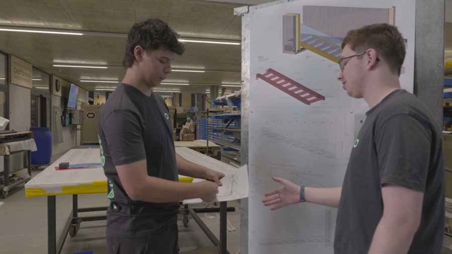 Zwei Lernende besprechen einen Plan in der Werkstatt von Delfosse